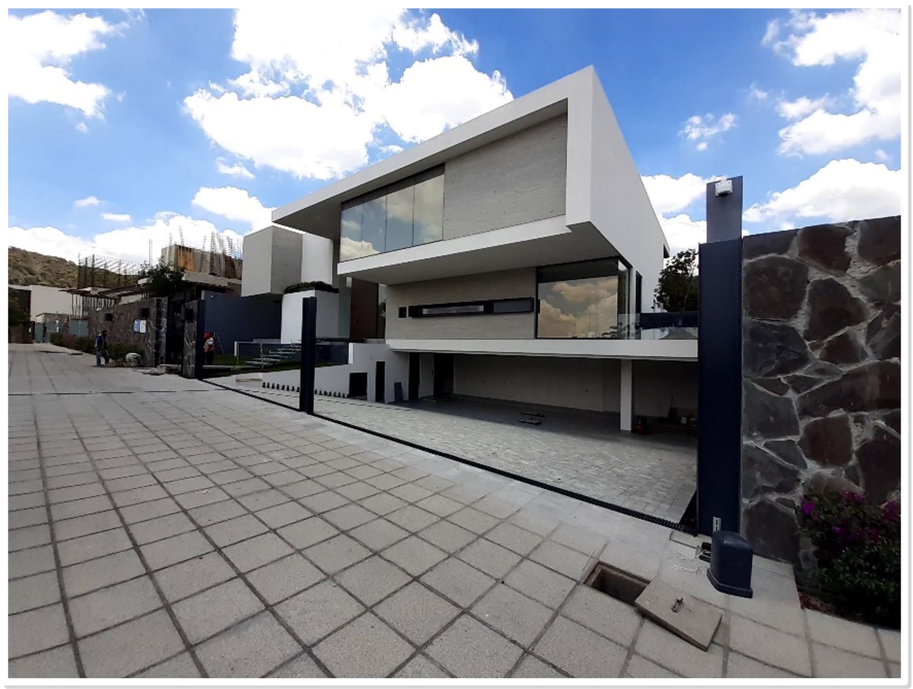 Casa moderna de dos niveles con fachada minimalista en blanco y gris, ventanales grandes, garage integrado y pavimento de adoquín