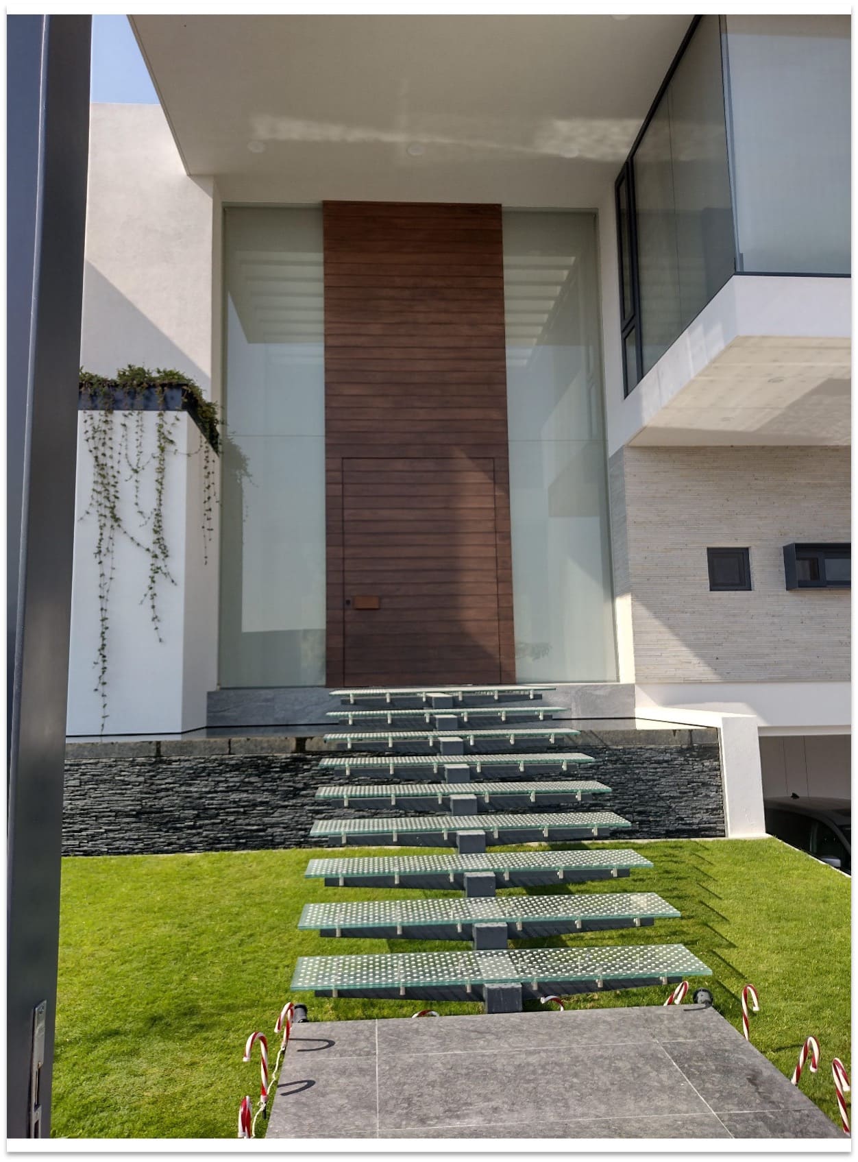 Puerta de ingreso principal en madera con diseño contemporáneo de tablillas horizontales, marco de cristal y acceso por escalones flotantes