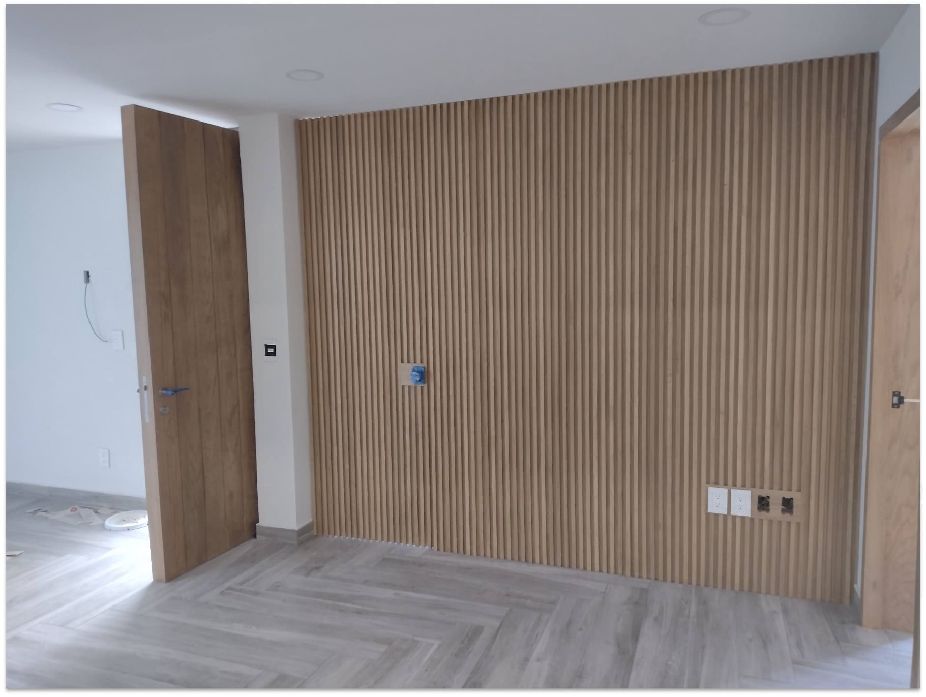 Habitación con pared completa de listones verticales de madera, puerta de madera con vetas naturales y contactos eléctricos integrados