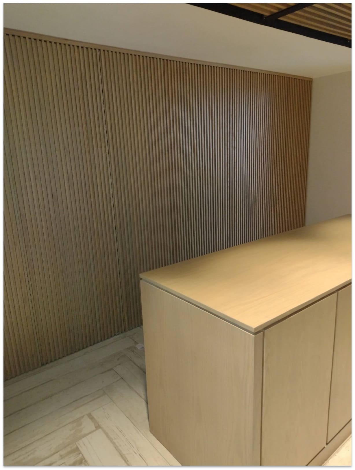 Mueble bajo de madera clara con puertas lisas y pared de fondo con listones verticales de madera en tono más oscuro