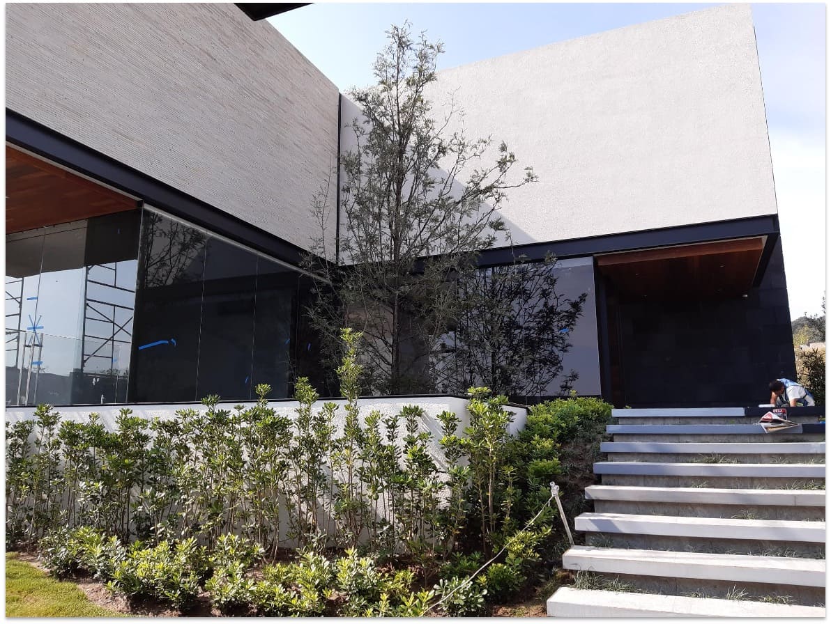 Exterior de casa moderna con fachada de listones horizontales de madera, ventanales grandes, escalones de concreto y jardín paisajístico